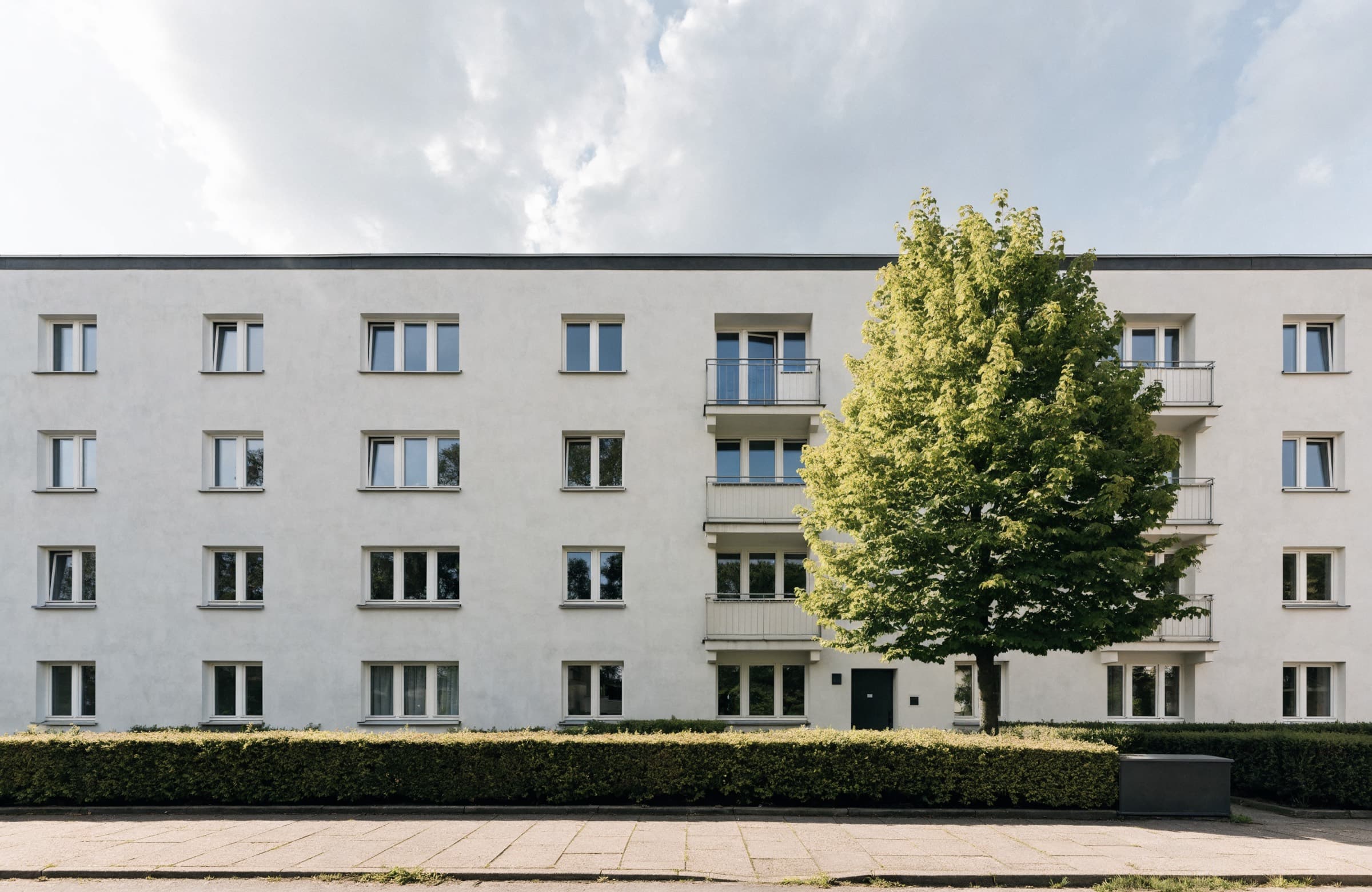 Viergeschossiges Mehrfamilienhaus mit heller Putzfassade und Vorgarten